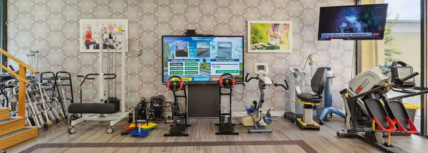 Rehabilitation gym with various exercise equipment and displays.